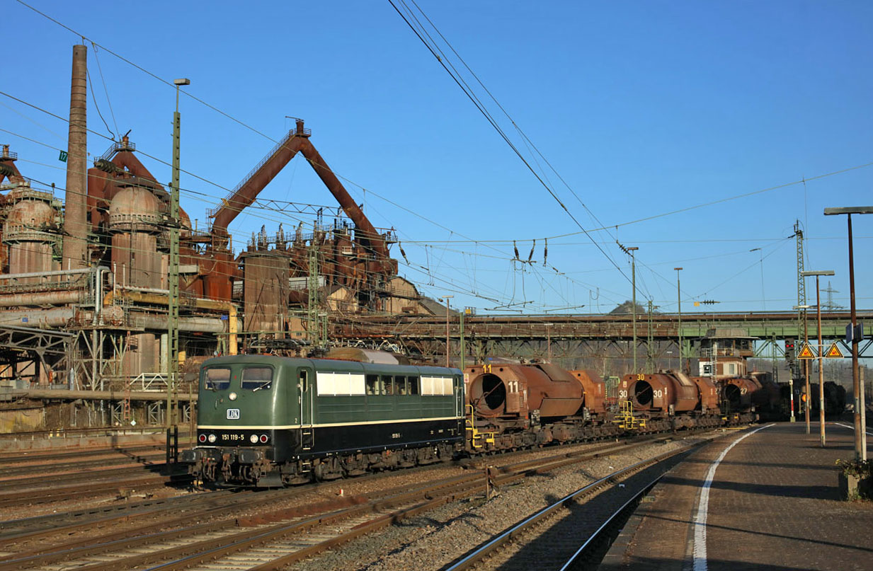 On 29 March 2021 Saar Rail used Bayernbahn 151 119 (rented via Leipziger Dampf KulTour) to haul liquid iron train 91305 from Dillingen Hochofen to Völklingen, here seen at arrival at Völklingen in front of the Unesco World Heratige Site of Völklinger Hütte (an old iron factory).